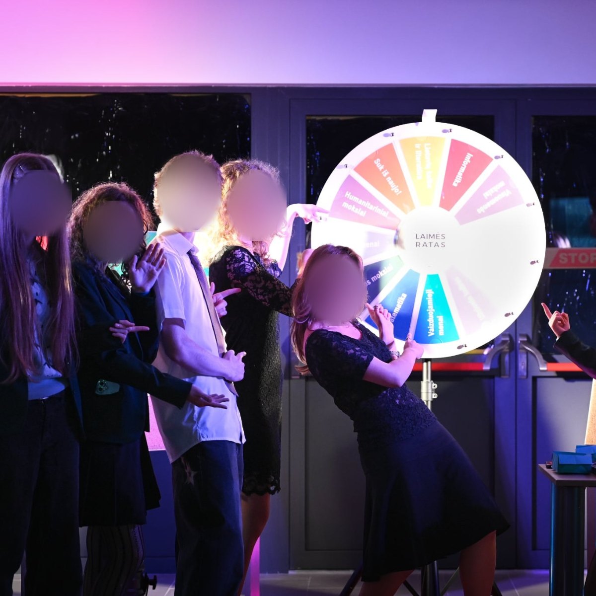 Group of people pointing at a colorful prize wheel of fortune at a school event